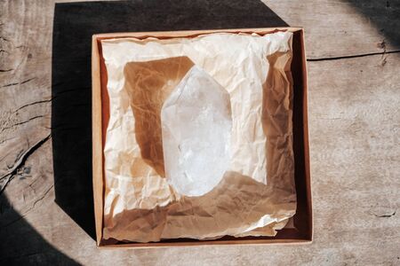 Quartz crystal in a kraft paper box on wooden background. Copy, empty space for text.の写真素材