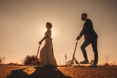 Silhouette wedding couple riding a on scooters along the road outside the city at sunset.の写真素材