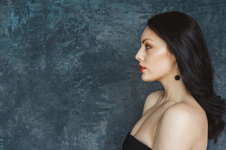 Fashionable portrait beautiful woman of a stylish brunette with red lips. Woman with long hair wearing black earrings. Set on gray backgroundの写真素材