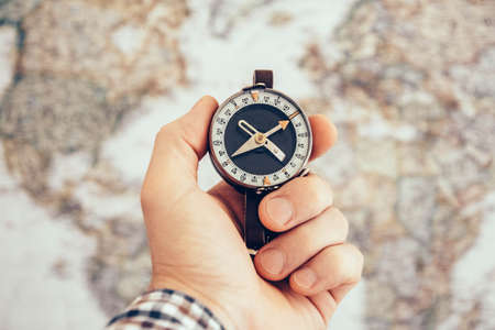 Close up of man hand holding vintage compass with world map as background. Travel and Business planning conceptの写真素材