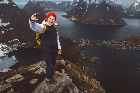 Man traveler taking self-portrait a photo with a smartphone hiking on Reinebringen mountain ridge in Norway lifestyle adventure travelingの写真素材