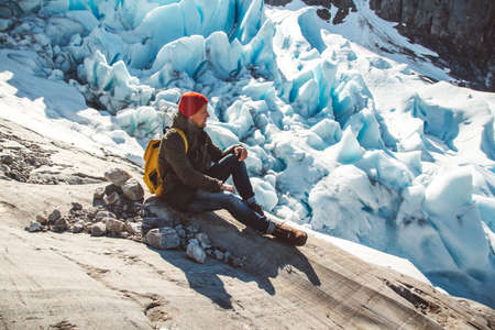 Traveler man with a yellow backpack wearing a red hat sitting on a rock on the background of a glacier and snow. Travel lifestyle conceptの写真素材