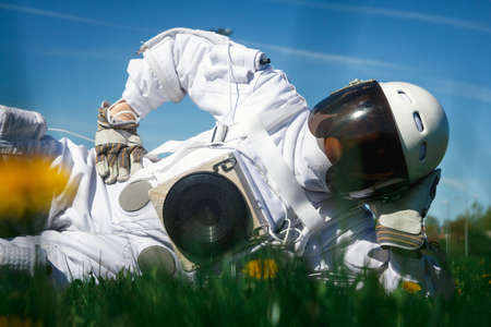 Futuristic astronaut in a helmet sits on a green lawn among flowers.の写真素材