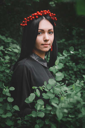 Beautiful girl in black dress and red earrings on the background of the forestの写真素材