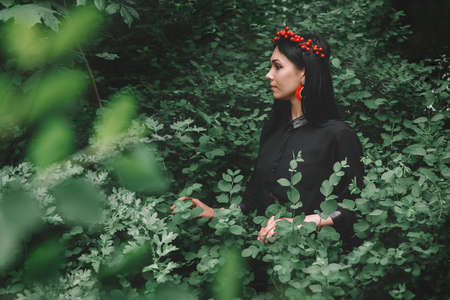 Beautiful girl in black dress and red decorations the background of the forest. Space for your text message or promotional contentの写真素材