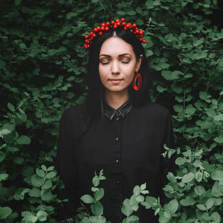 Beautiful girl with her eyes closed in black clothes and red earrings on the background of the forestの写真素材