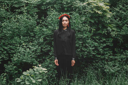 Beautiful girl with her eyes closed in black clothes and red earrings on the background of the forestの写真素材