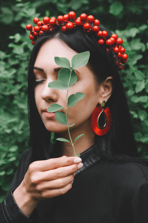Beautiful girl with black hair and red accessories that holds a leaf in her hand near her face...