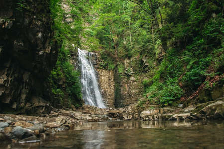 Waterfall with a lake among rocks and forestの写真素材