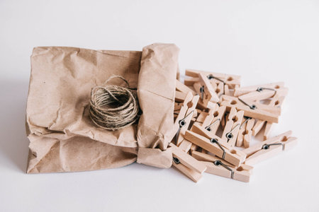Wooden clothespins in paper bag with rope on white background. View from above. Place for your text