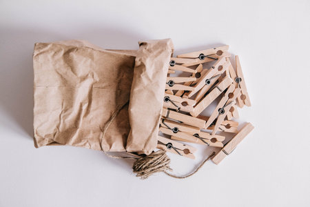 Wooden clothespins in paper bag with rope on white background. View from above. Place for your text