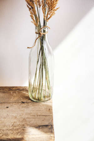 Still life of a bouquet of dried flowers in a glass bottle on a wooden table. Place for text or advertisingの写真素材