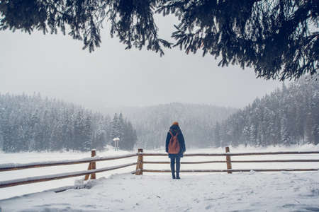 Beautiful girl with a backpack on a background of snow-covered forest. Travel lifestyle concept. Shoot from the backの写真素材