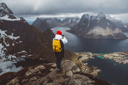 Man traveler taking photo with a smartphone hiking on Reinebringen mountain ridge in Norway lifestyle adventure travelingの写真素材