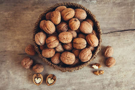 Walnuts in a round wicker basket on a wooden background. Top view. Copy, empty space for textの写真素材