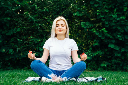 Beautiful blonde girl in headphones and smartphone in hands listens to music lying on green...