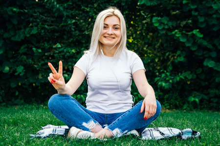 Beautiful blonde girl in headphones and smartphone in hands listens to music lying on green background. Lifestyle concept. Copy, empty space for text.の写真素材