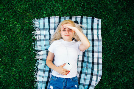 Beautiful blonde girl in headphones and smartphone in hands listens to music lying on green background. Lifestyle concept. Copy, empty space for text.の写真素材