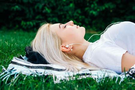 Beautiful blonde girl in headphones and smartphone in hands listens to music lying on green background. Lifestyle concept. Copy, empty space for text.の写真素材