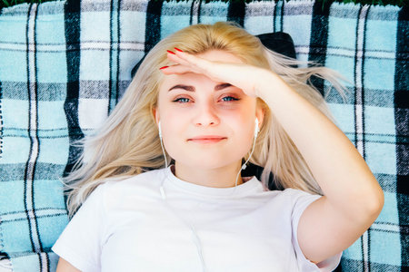 Portrait of beautiful blonde girl in headphones listens to music lying on rug background. Copy, blank space for textの写真素材