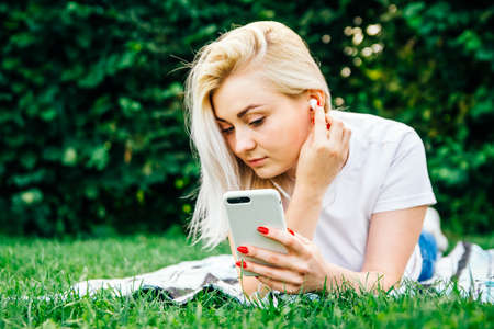 Beautiful blonde girl in headphones and smartphone in hands listens to music lying on green background. Lifestyle concept. Copy, empty space for textの写真素材