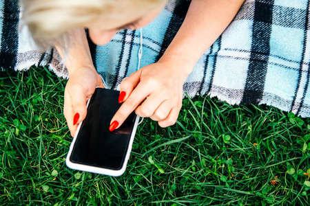 Beautiful blonde girl in headphones and smartphone in hands listens to music lying on green background. Lifestyle concept. Copy, empty space for textの写真素材