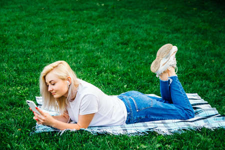 Beautiful blonde girl in headphones and smartphone in hands listens to music lying on green background. Lifestyle concept. Copy, empty space for textの写真素材