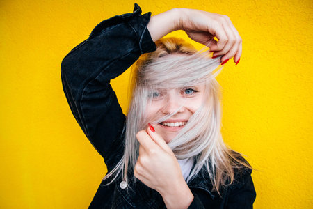 Portrait of beautiful blonde girl in a black jacket smiling and holding her hair against a...