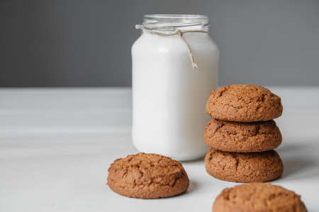 Milk in a glass jar and oatmeal cookies on a white table background. Copy, empty space for textの写真素材