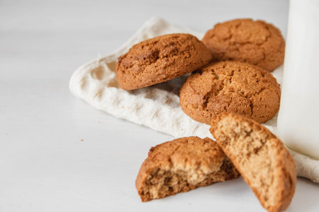 Milk in glass jar and oatmeal cookies near napkin on white table background. Copy, empty space for...