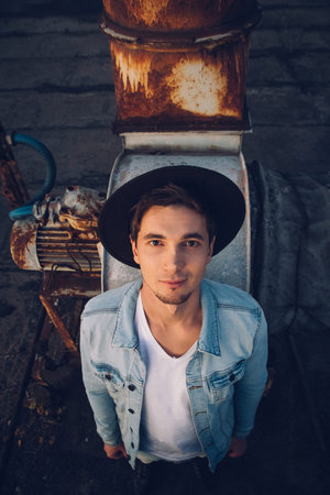 UUrban man with hat against the background of the city. Wearing white shirt and jeans. Old neglected...