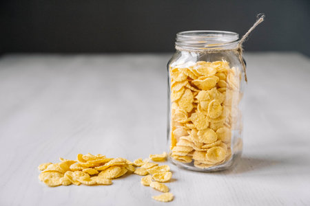 Corn flakes in a glass jar on white wooden surface. Place for your text.の写真素材