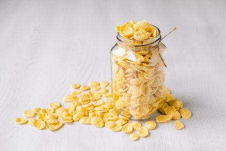 Corn flakes in a glass jar on white wooden surface. Place for your text.