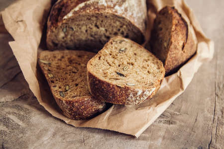 Brown fresh bread with seeds are cut into pieces on old wood background. Top view, copy space.の写真素材