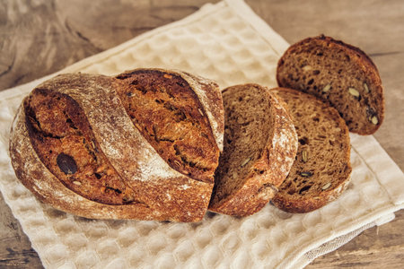 Brown fresh bread with seeds are cut into pieces on old wood background. Copy, empty space for text.
