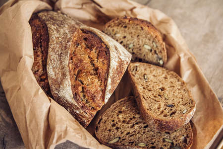 Brown fresh bread with seeds are cut into pieces on old wood background. Top view, copy space.の写真素材