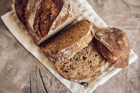 Brown fresh bread with seeds are cut into pieces on old wood background. Top view, copy space.