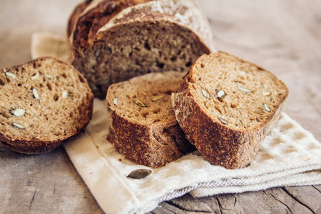 Brown fresh bread with seeds are cut into pieces on old wood background. Top view, copy space.