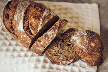 Brown fresh bread with seeds are cut into pieces on old wood background. Top view, copy space.