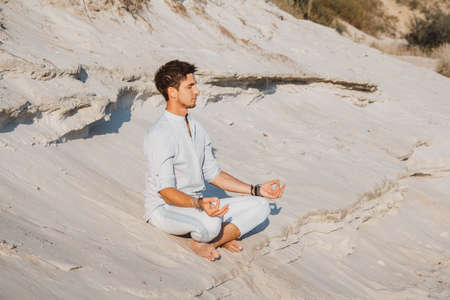 Young handsome man in light clothing sits in the desert. Concept of freedom relaxation. Place for text or advertising.の写真素材