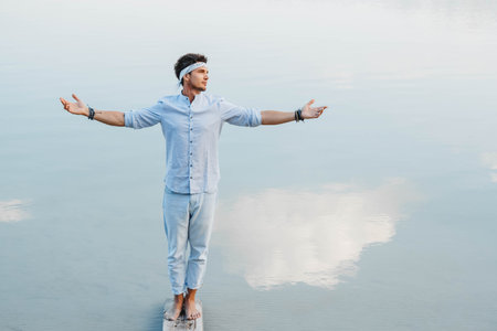 Man handsome dressed in light clothes looks at the water reflex of blue sky. Shoot from the back. Concept of freedom relaxation. Place for text or advertising.の写真素材