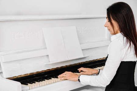 Beautiful woman dressed in a white dress with a black corset lies on the floor near white piano playing on the keys. Place for text or advertising. View from above.の写真素材
