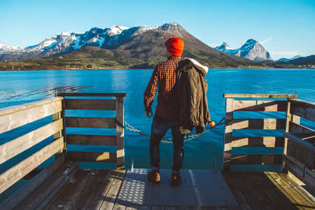 Traveler man sits in a boat near a wooden pier on a background of a mountain lake. Place for text or advertising.の写真素材