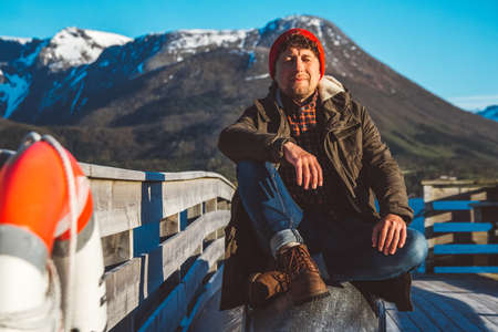 Traveler man sits in a boat near a wooden pier on a background of a mountain lake. Place for text or advertising.の写真素材