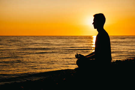 Silhouette of a man in meditation pose on beach on sea background and sunset. Concept of freedom relaxation. Place for text or advertising.の写真素材