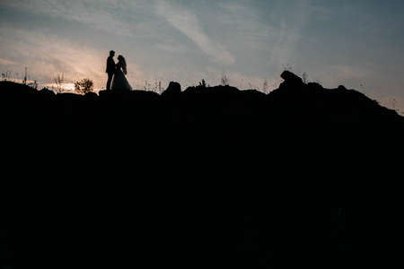 Silhouettes of a young couple lovers at sunset on dramatic sky background. Place for text or advertising.の写真素材