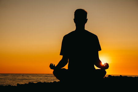 Silhouette of a man in meditation pose on beach on sea background and sunset. Concept of freedom...