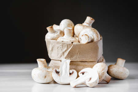 Mushrooms champignons in paper bag on a white wooden table. Place for text or advertising.の写真素材