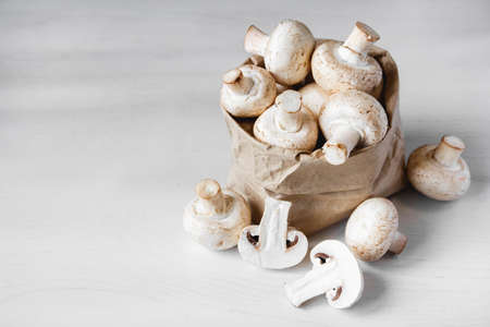 Mushrooms champignons in paper bag on a white wooden table. Place for text or advertising.の写真素材
