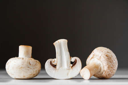 Mushrooms champignons lie in a row on a white table on a dark background. Place for text or advertising. Design border.の写真素材